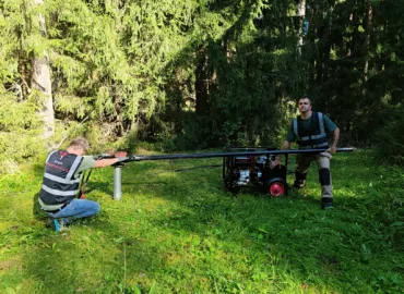 Two workers installing a screw pile in the ground with Iron-Mechanics handheld helical pile driver