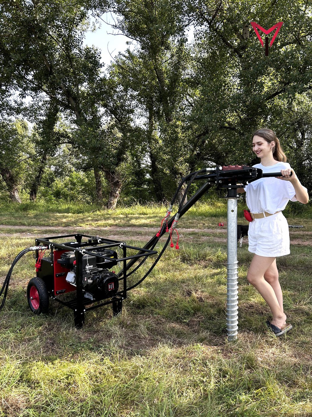 Woman operating a manual hydraulic ground screw driver for screw pile installation in the field